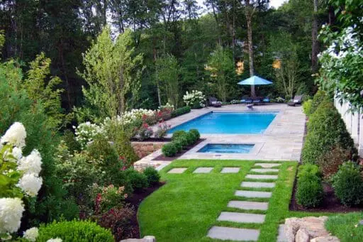 Boston-area plunge pool and spa surrounded by a stone patio, manicured lawn, flowering hydrangeas, and layered landscape plantings