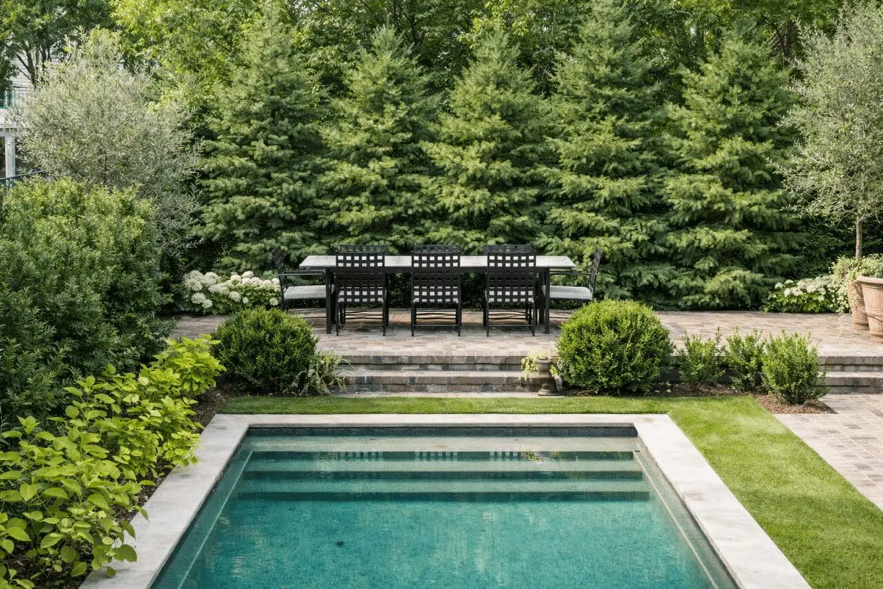 A dense backdrop of Eastern White Pine creates a soft, natural privacy screen, framing the pool terrace while maintaining a distinctly New England landscape character.