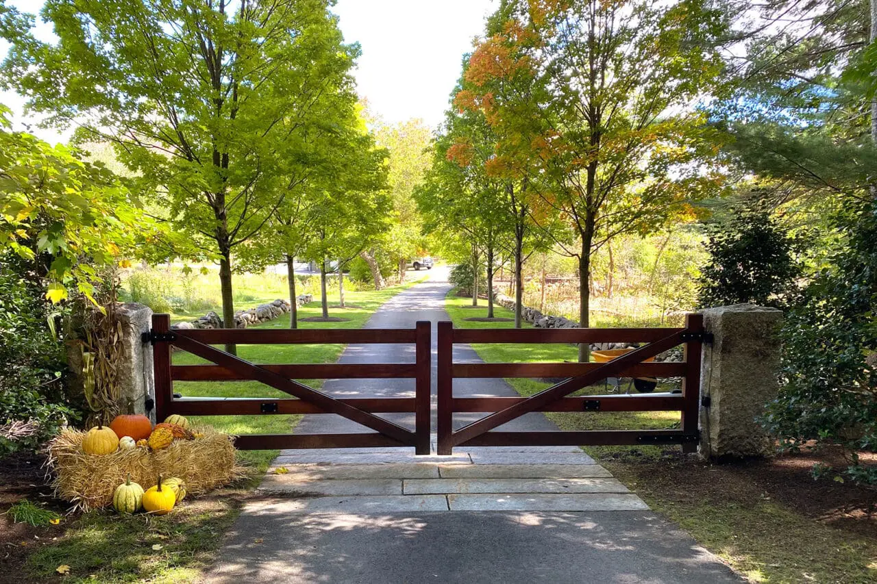 Carlisle, MA - A handcrafted wood gate frames a tree-lined drive, creating a formal yet rural arrival sequence that sets the tone for this historic New England estate.