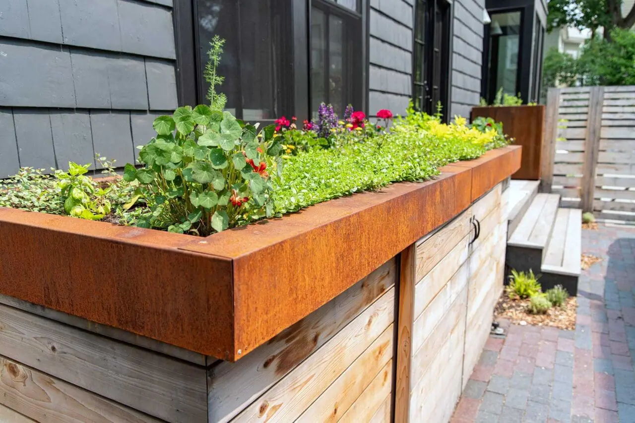 Cambridge, MA - Weathering steel planters paired with custom wood cabinetry create a functional outdoor kitchen zone, with edible plantings above and concealed storage for garbage and recycling bins below. Photo credit: Dan Kaplan