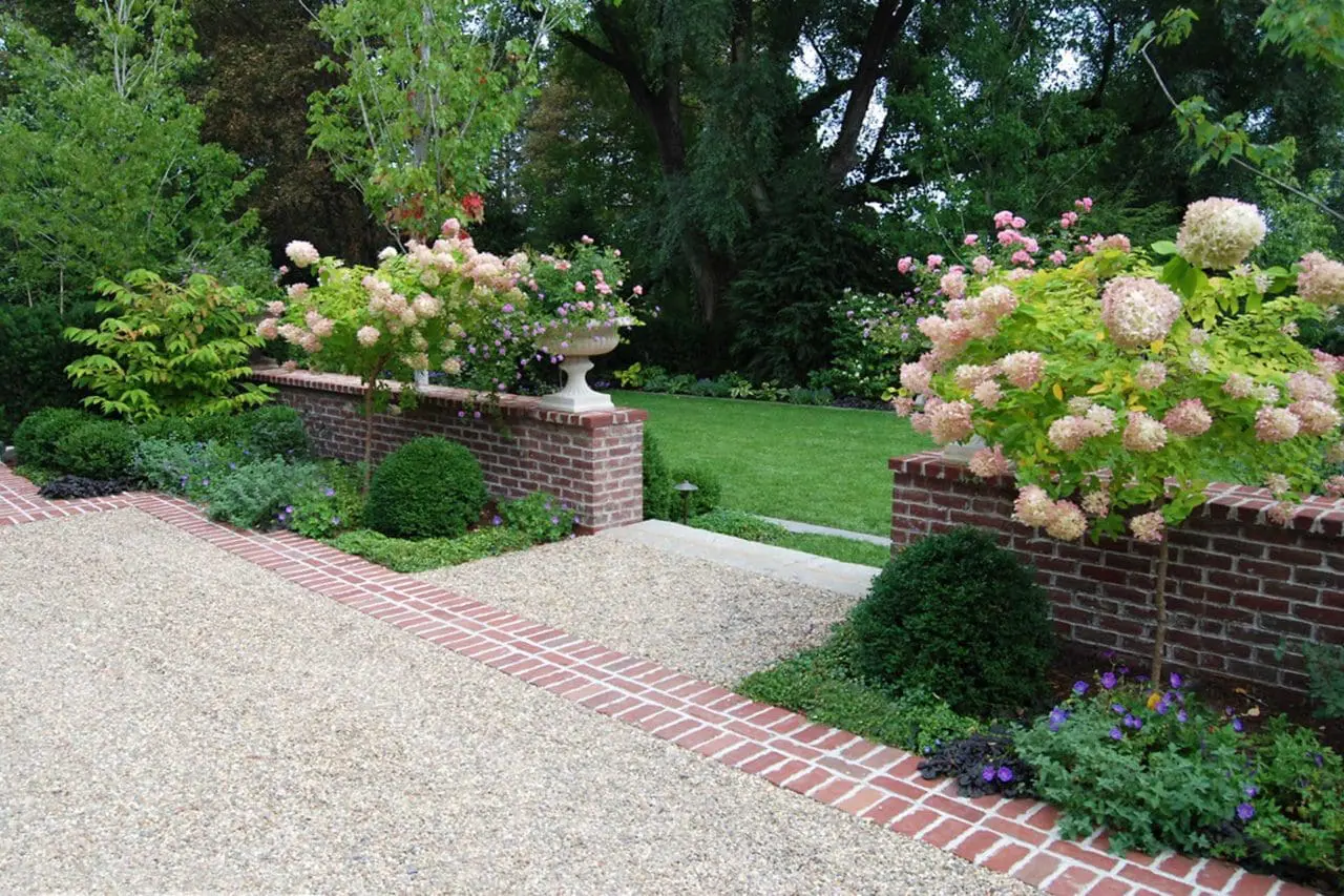 Belmont, MA - A classic brick wall provides a boundary between the chip-seal parking court and lawn. Late summer annuals, perennials, and hydrangea trees pop with color.