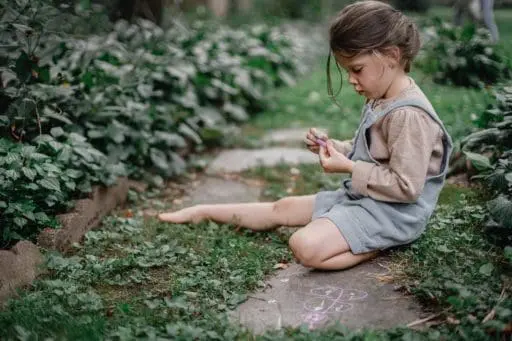 A child sits along a garden path drawing with chalk, capturing how time spent at home can turn the landscape into a place for creativity and everyday discovery.