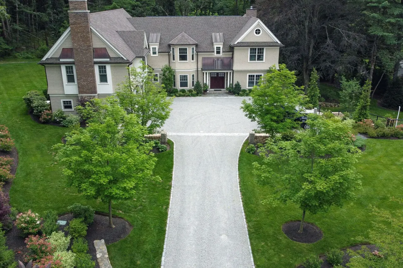 Concord, MA - A symmetrical gravel driveway is framed by granite pillars, creating a formal, balanced approach that emphasizes proportion and long-term durability.