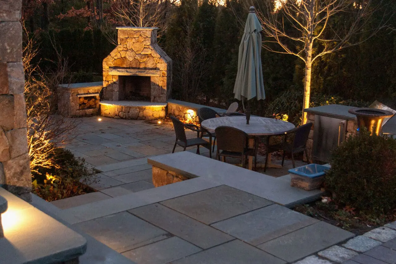 Accent lighting defines the stone patio and fireplace, creating a warm, inviting outdoor gathering space.