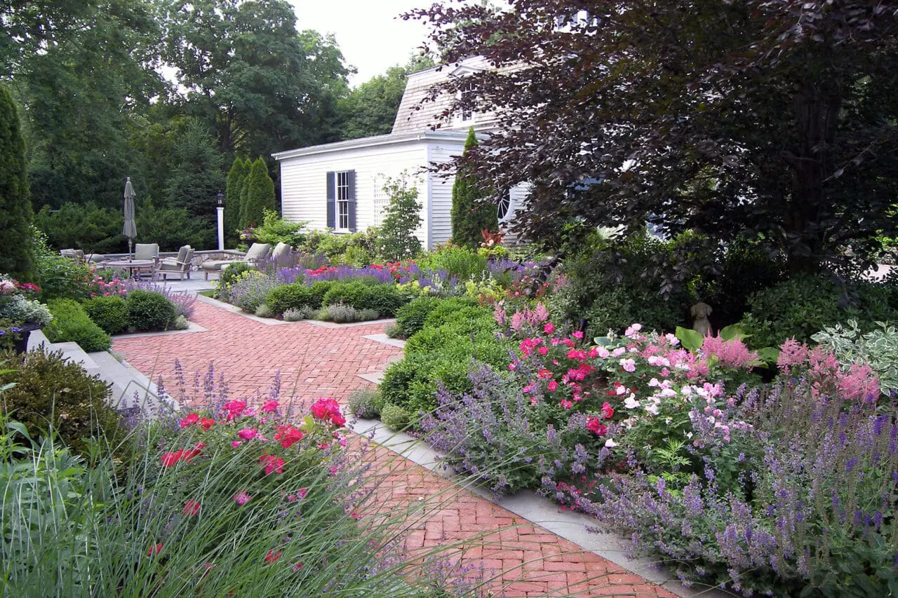 A brick garden path flows through lush perennials, blending structure with classic estate-style planting.