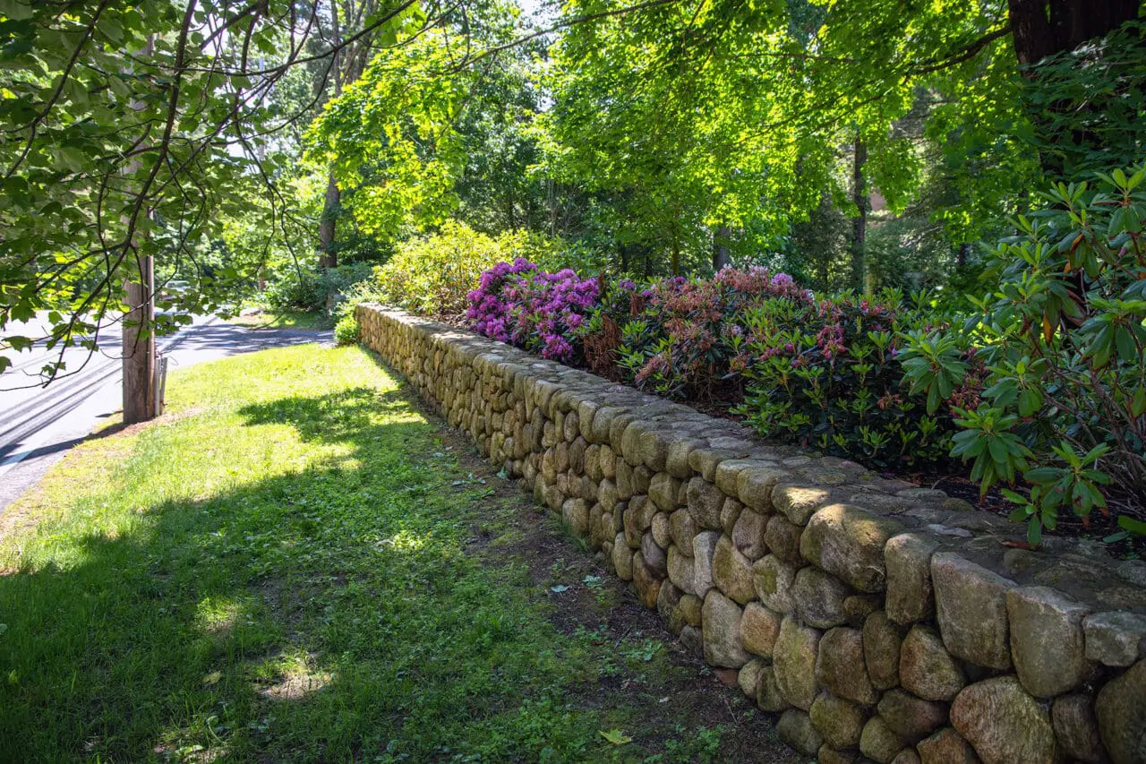 A dry-laid fieldstone wall establishes a clear edge along the neighboring street using large, irregular stones.