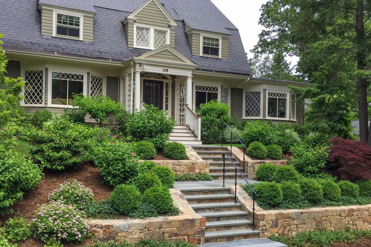 Newton, MA - Fieldstone retaining walls paired with granite steps guide movement along a hillside path, using shrubs and hedges to stabilize slopes and frame the route.