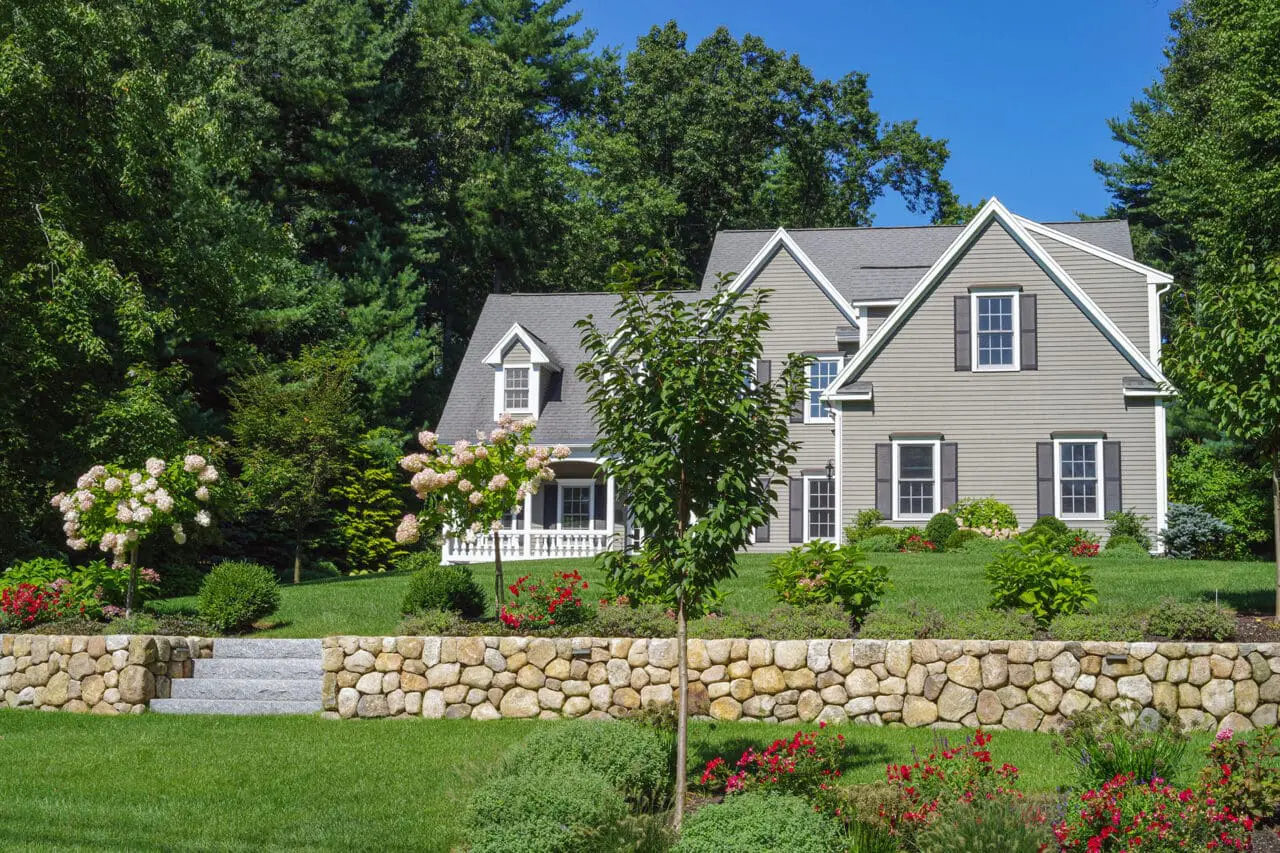 Stow, MA - A low fieldstone retaining wall manages a gentle grade change in the front yard, its informal stonework complemented by shrubs that ease the transition between lawn and planting areas.