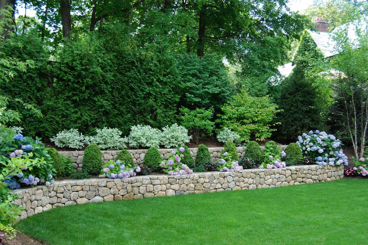 Multi-level natural stone garden walls define the grade and create a series of planted terraces, while a winding path connects the different elevations through the landscape.