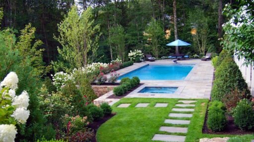 Boston-area plunge pool and spa surrounded by a stone patio, manicured lawn, flowering hydrangeas, and layered landscape plantings