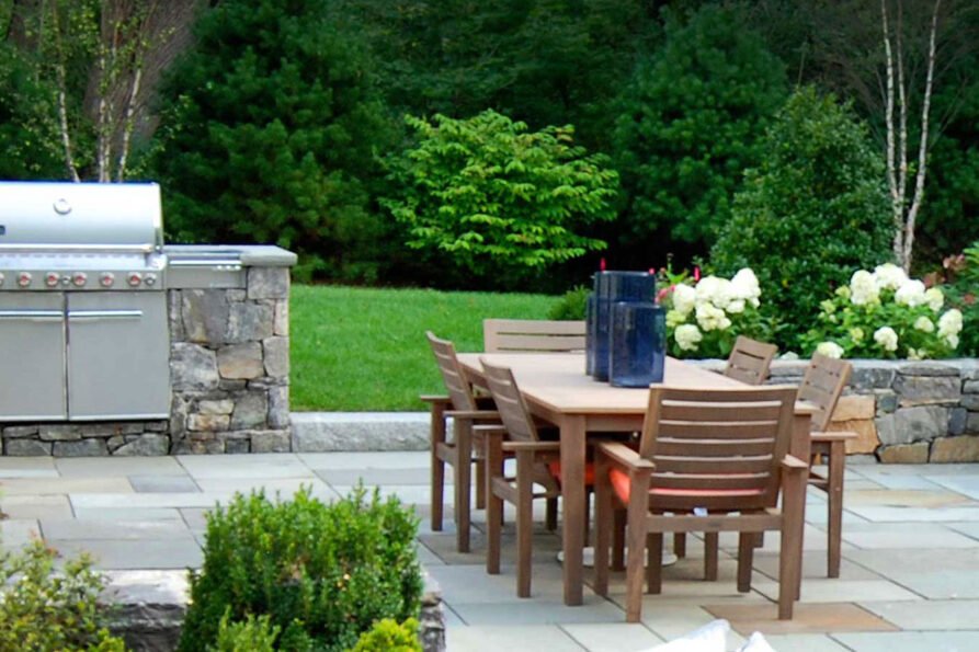 A thoughtfully designed outdoor dining area creates a comfortable place for meals and entertaining, with well-planned seating, circulation, lighting, and surrounding plantings helping the space feel connected to the landscape.