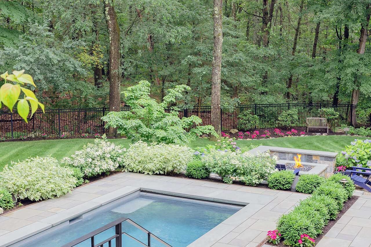 Wellesley, MA - The pool terrace and fire feature are set within layered planting beds and backed by mature trees, giving the landscape a private, resort-like feel. photo credit: Michael J Lee