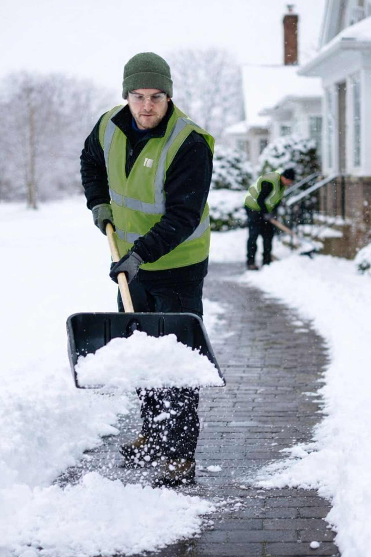 A crew member shovels fresh snowfall from a curved entry walk, providing reliable walkway snow removal and ice control in Boston neighborhoods.