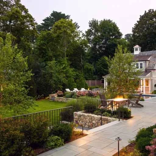 Wayland, MA - A bluestone terrace with evening lighting and a fire feature turns a sloped property into a warm, elevated outdoor living area.