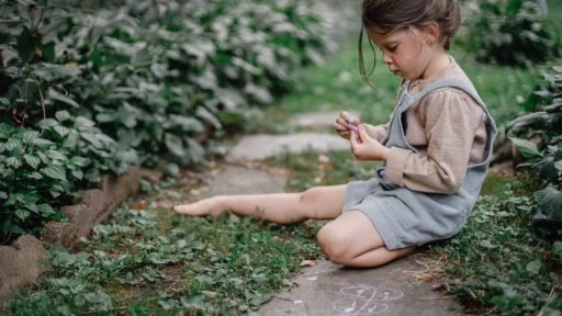 A child sits along a garden path drawing with chalk, capturing how time spent at home can turn the landscape into a place for creativity and everyday discovery.