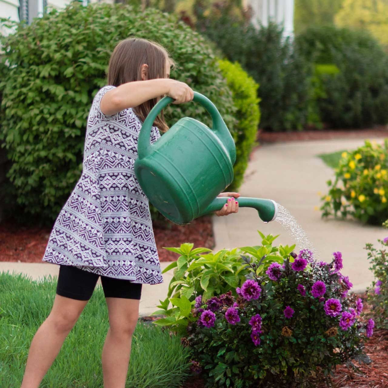 A child waters purple flowers beside the home, capturing the hands-on pleasure of gardening and caring for a landscape at home.