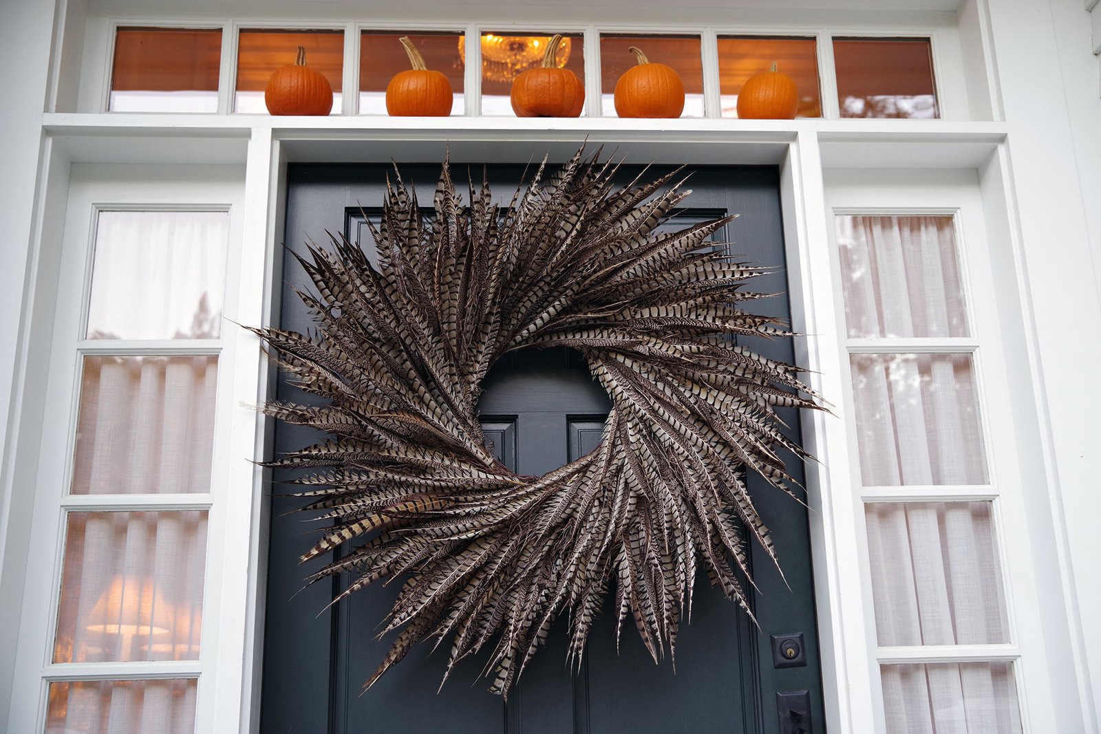 A unique feather wreath introduces texture and movement, offering a modern seasonal accent that stands out against a neutral front door.