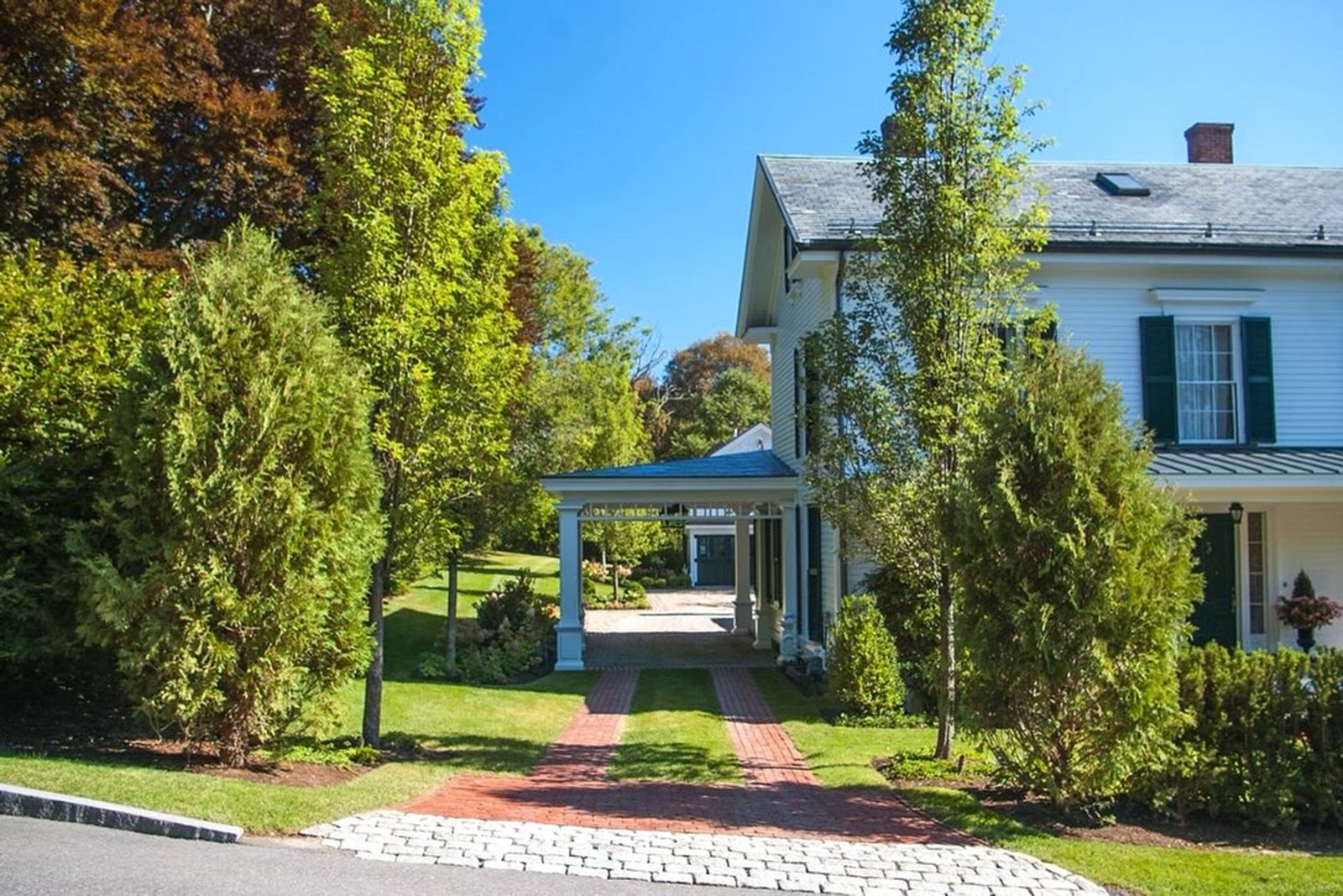 Brick ribbons guide vehicles along this driveway, transitioning to a cobblestone apron that enhances the colonial home approach with pattern and contrast.