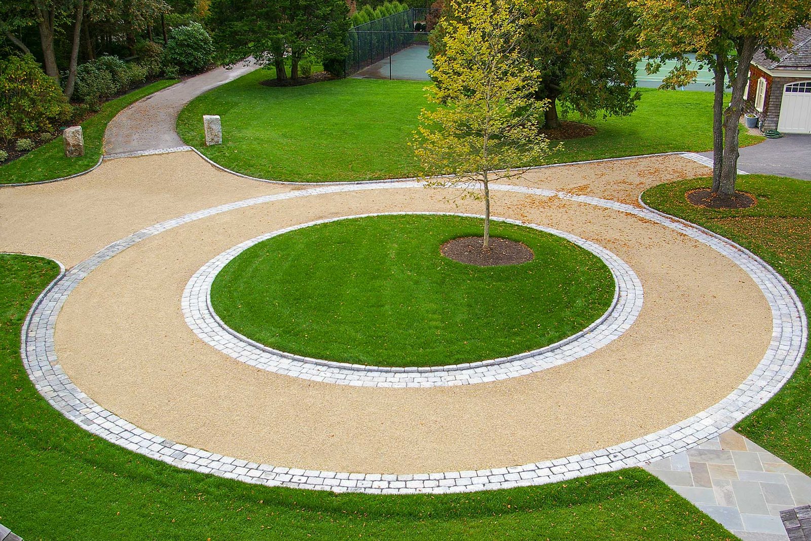 Duxbury, MA - This circular gravel driveway features a cobblestone ring and planted center island, organizing traffic flow while adding visual focus and texture.