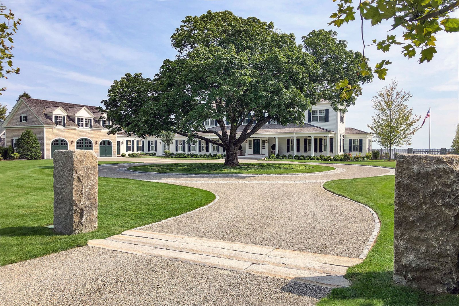 A formal circular gravel driveway anchors a grand estate entry, framed by stone pillars that add structure, durability, and a strong sense of arrival without feeling overly rigid.
