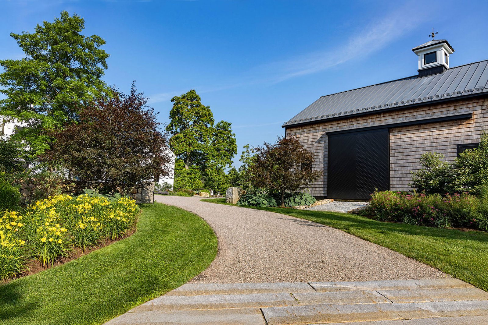 Carlisle, MA - A gently curved gravel driveway complements barn-style architecture, using soft lines and naturalistic planting to guide arrival while maintaining permeability and a relaxed, rural character.