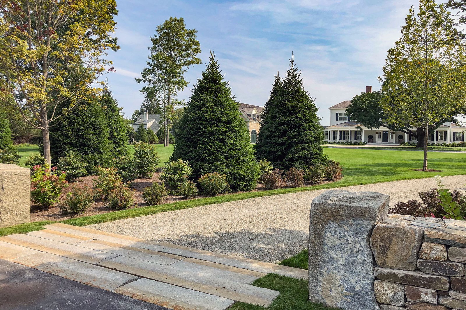 This curved gravel driveway pairs boxwood and hydrangea borders, softening the approach to a colonial home with seasonal interest and defined geometry.