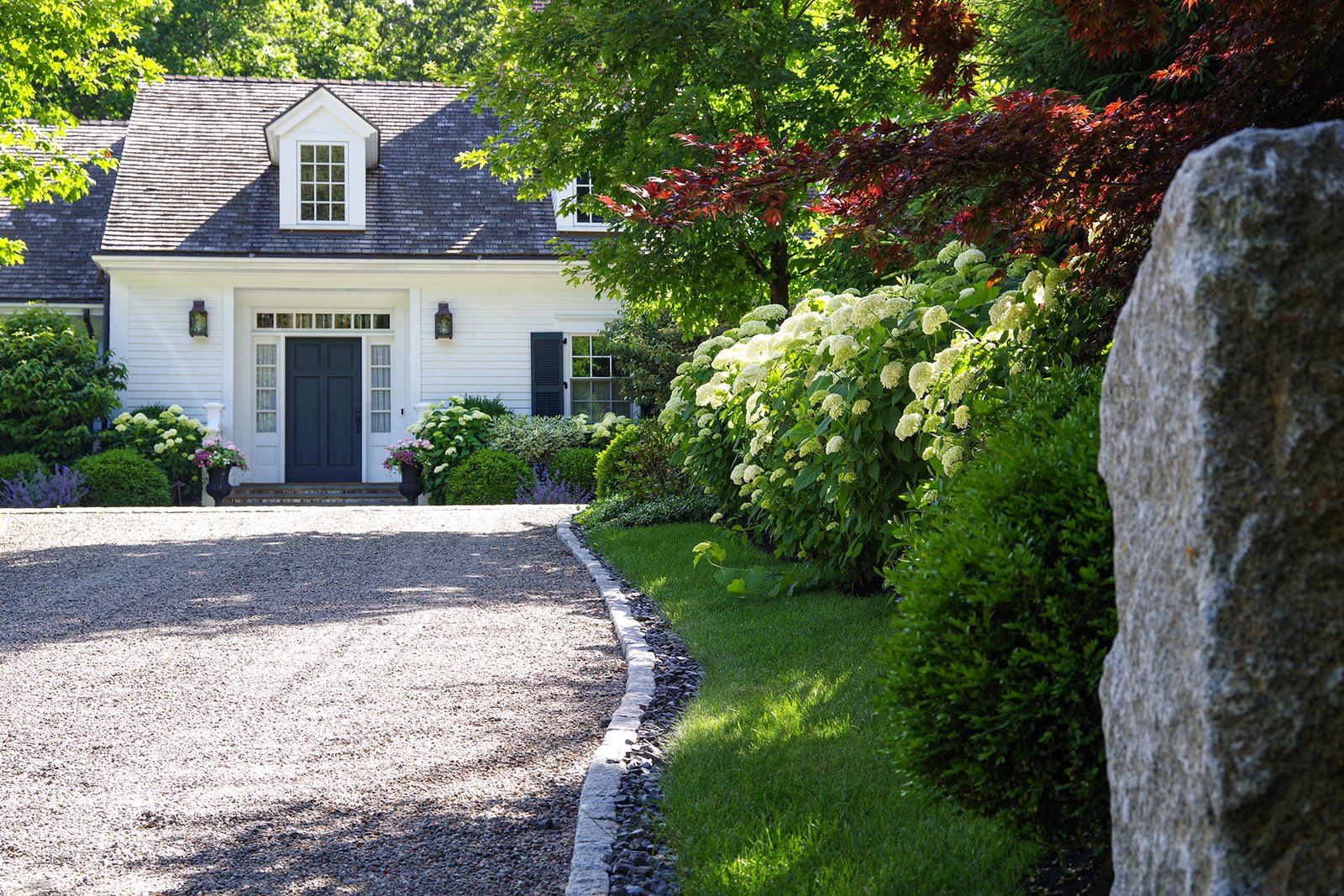 Weston, MA - Granite edging frames a curved gravel driveway beneath mature trees, preserving roots while maintaining clean lines and controlled edges.
