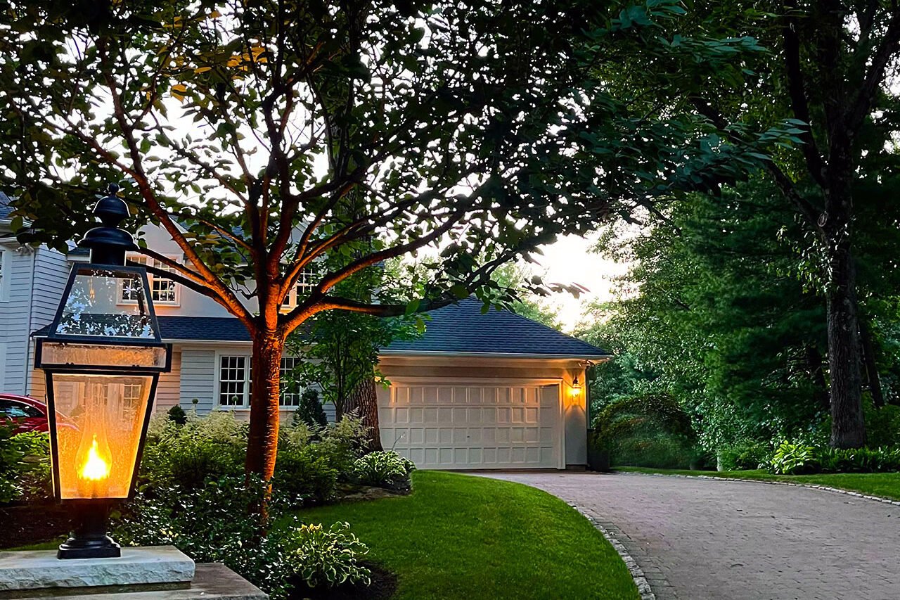 Curved pavers and stone lighting columns define this driveway, enhancing visibility and creating a welcoming evening arrival with balanced illumination and structure.