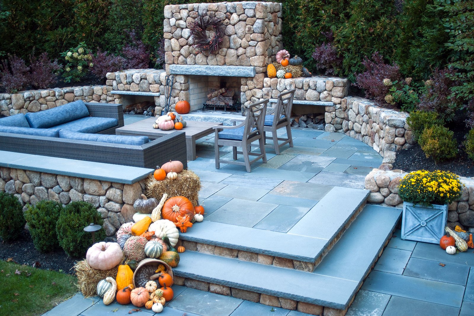 Weston, MA - Pumpkins and hay bales surround a fieldstone fireplace on the patio, extending autumn style into outdoor living and entertaining spaces.