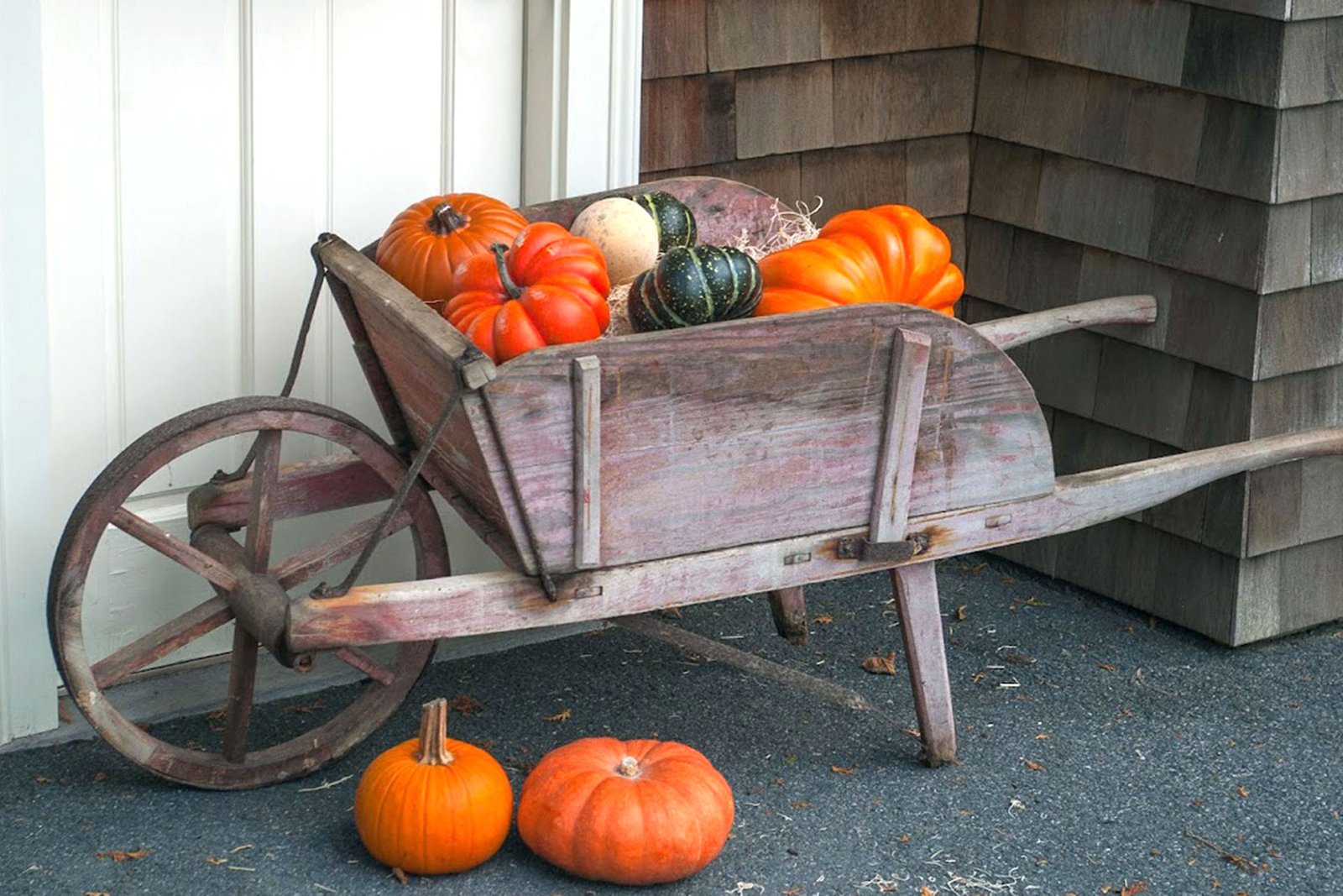 A rustic wooden wheelbarrow overflowing with pumpkins and gourds adds farmhouse charm and flexible fall personality to the entry.