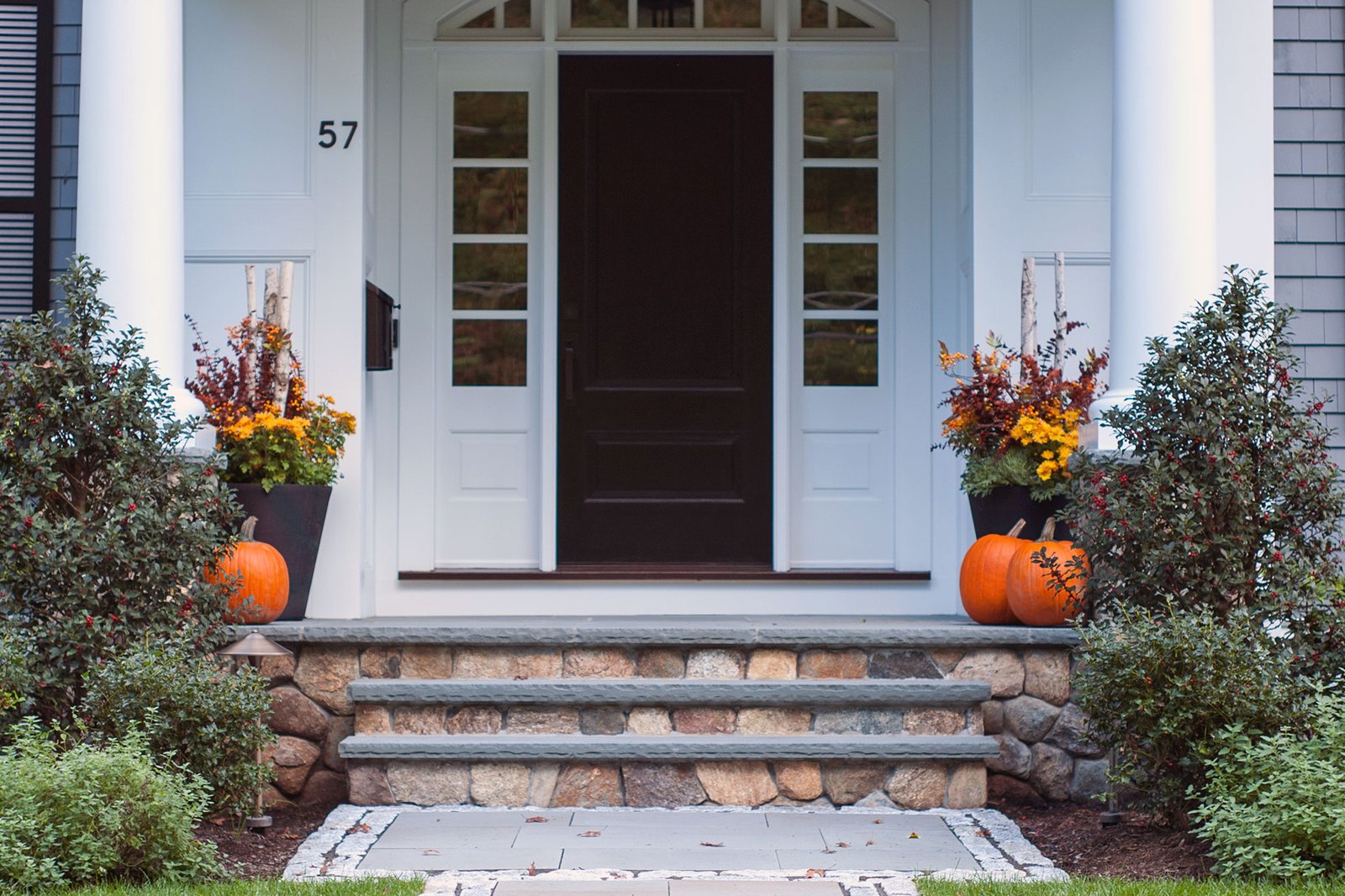 Symmetrical entry planters with birch branches, mums, and pumpkins line stone steps, creating balance and strong fall curb appeal.