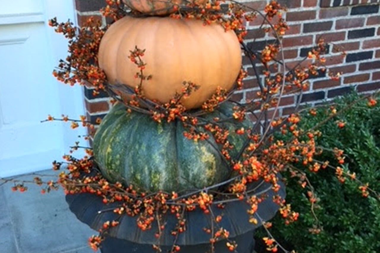 A tiered pumpkin topiary rising from an urn delivers vertical drama and playful fall style, perfect for making a bold entry statement.