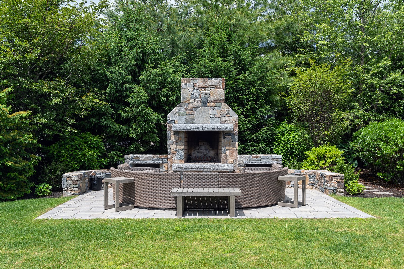 This classic stone outdoor fireplace in Dover, MA features curved seating that encourages conversation while providing warmth and a timeless New England focal point.