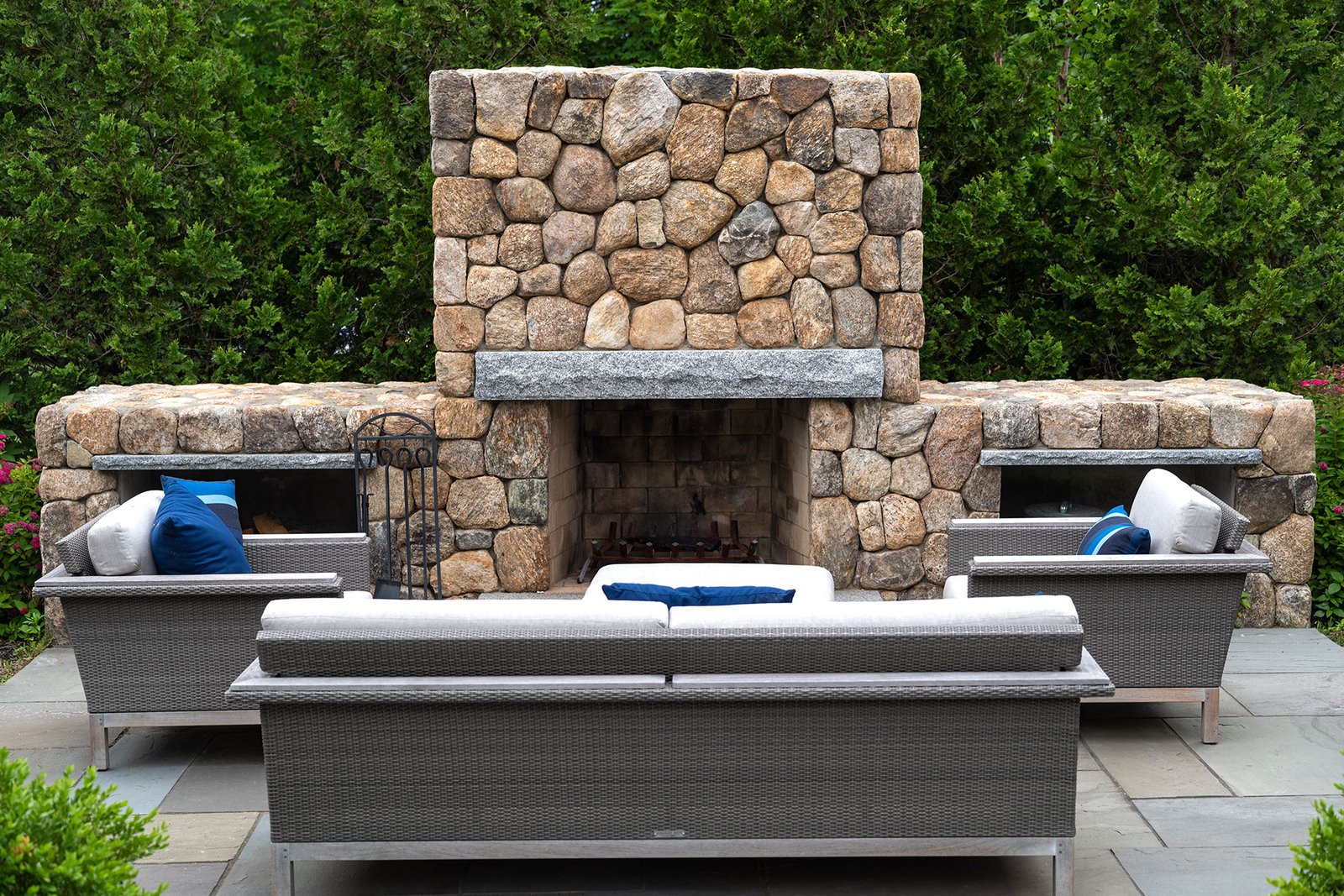 A fieldstone outdoor fireplace with integrated seating walls creates a protected gathering area, offering warmth, enclosure, and a natural transition between patio and garden.