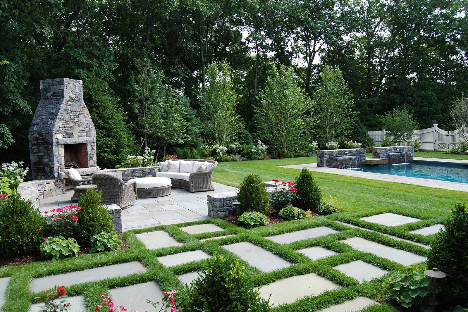 A natural stone outdoor fireplace near the pool creates a strong visual anchor, combining warmth, texture, and architectural presence to elevate the entire outdoor living area in Dover, MA.