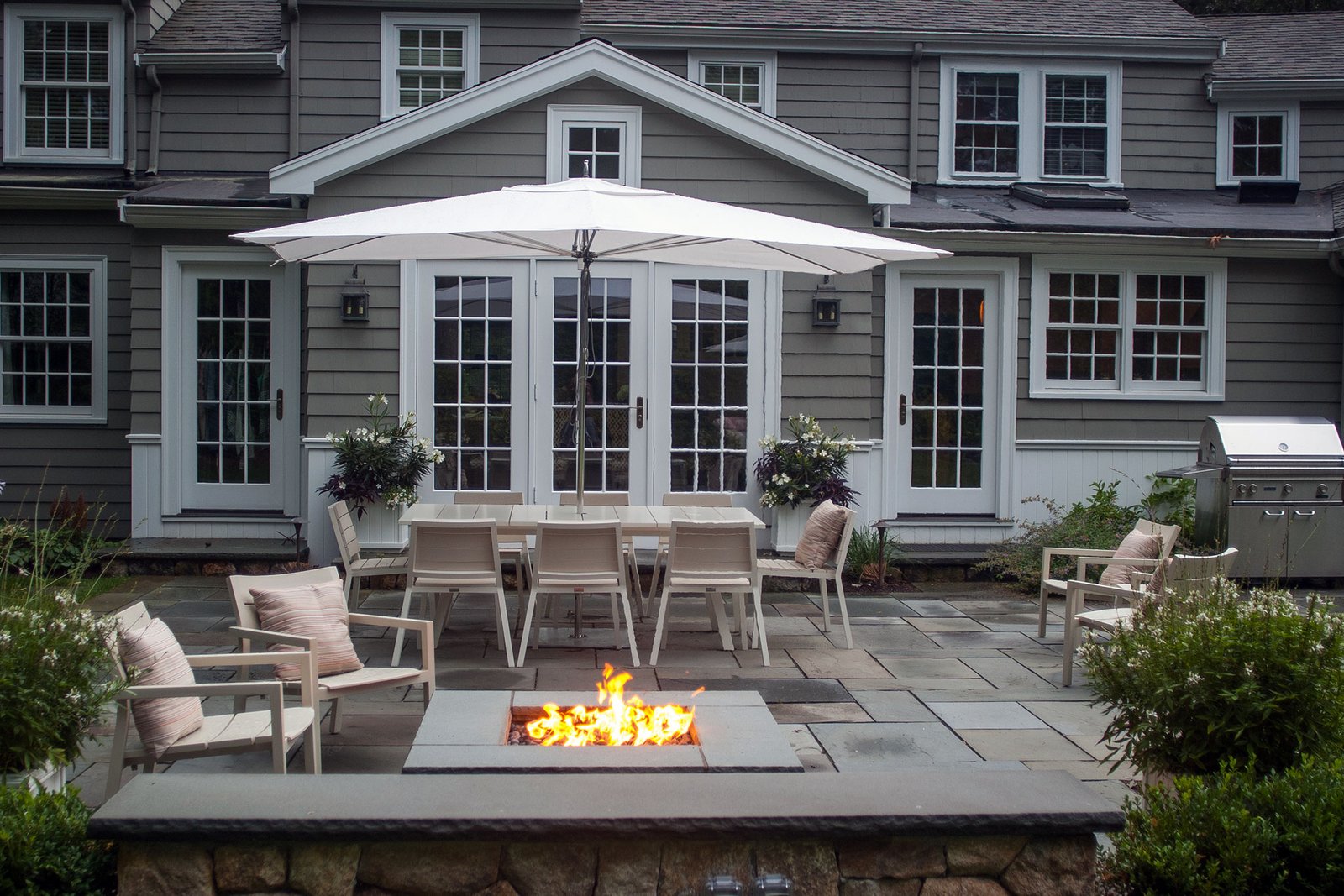 This rectangular stone fire pit enhances an outdoor dining patio by providing ambient warmth and atmosphere, making the space more inviting for longer meals and evening gatherings.