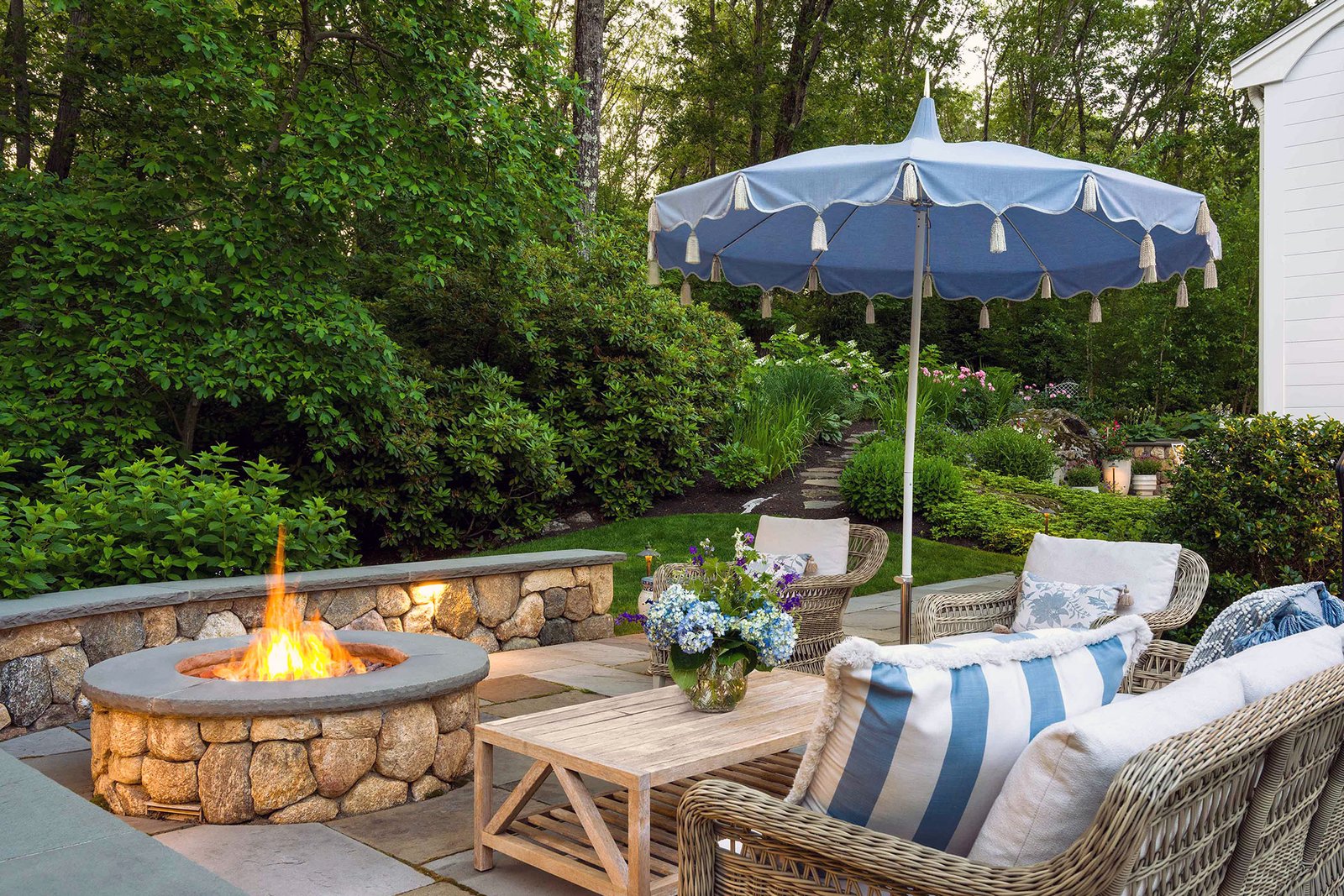 A round stone fire pit forms the center of this garden seating area, encouraging conversation while softening the hardscape with curved lines that complement surrounding plantings.