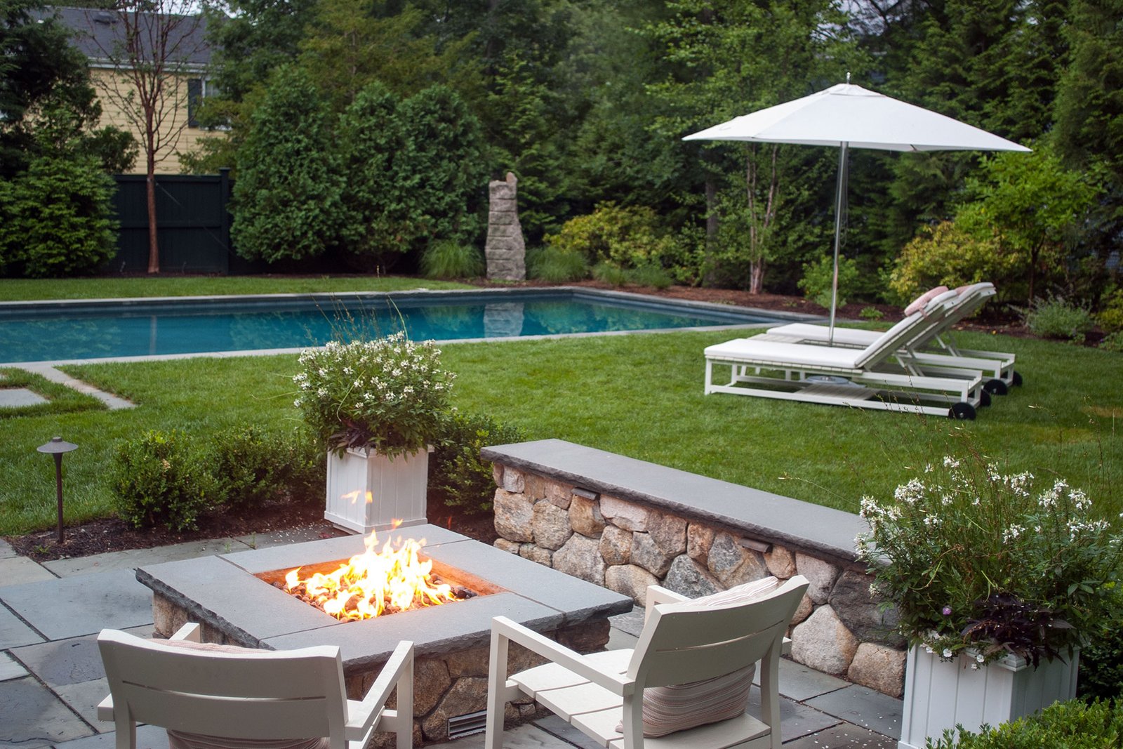 This stone fire pit near the pool is paired with a low seating wall, providing warmth, safety, and a natural gathering spot that balances hardscape structure with open views of the landscape.