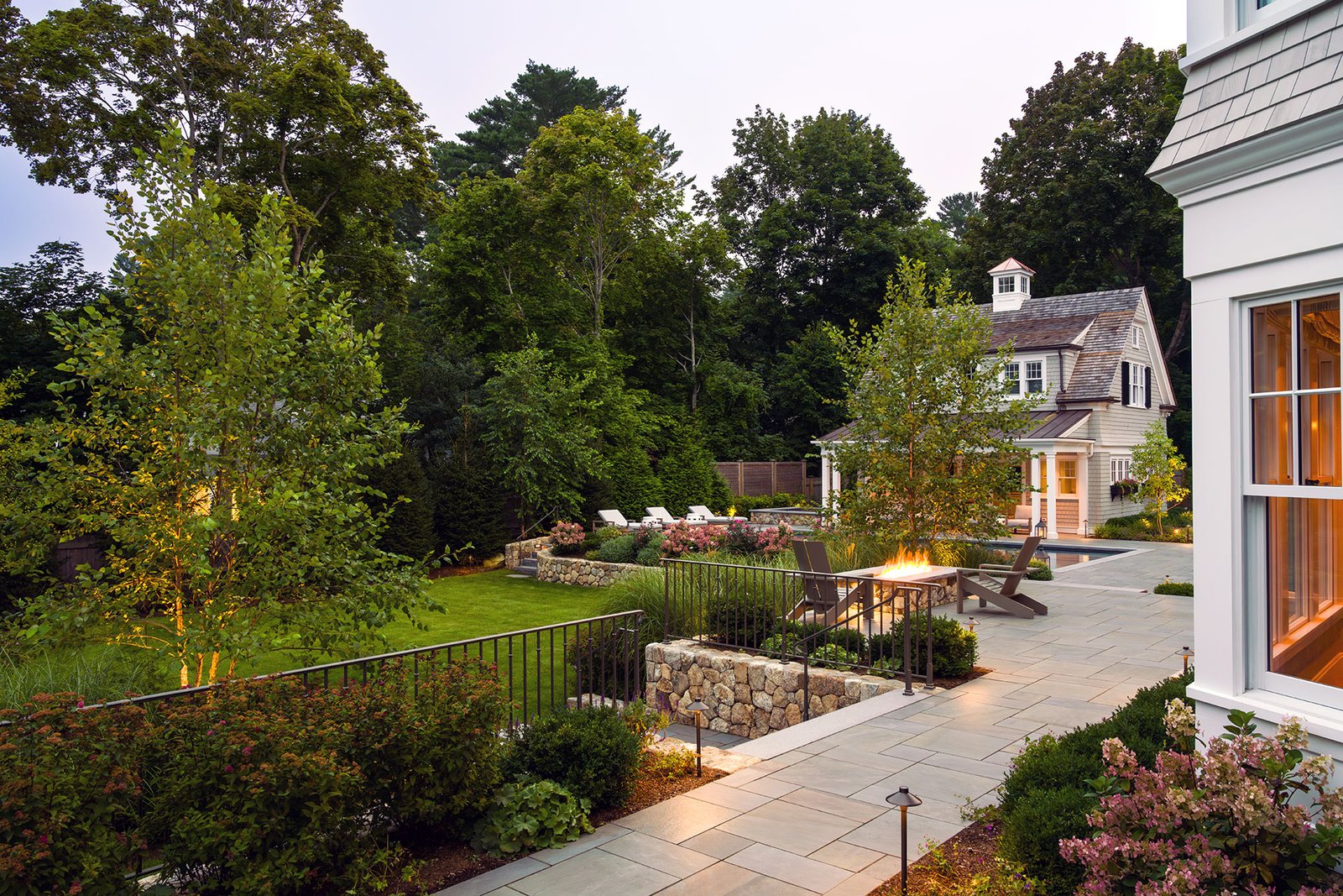 A terraced stone fire pit in Duxbury, MA uses retaining walls to define seating, manage grade changes, and create a warm gathering space that feels intentional, comfortable, and well integrated into the landscape.