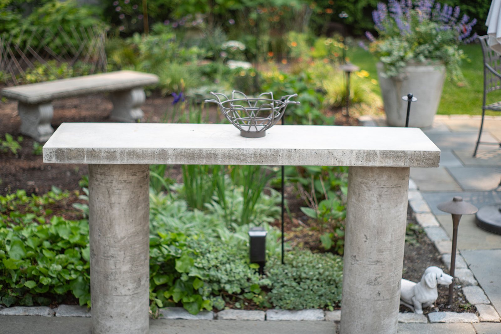 A stone console bench provides both sculpture and function, offering a refined resting spot that blends seamlessly into the surrounding landscape setting.
