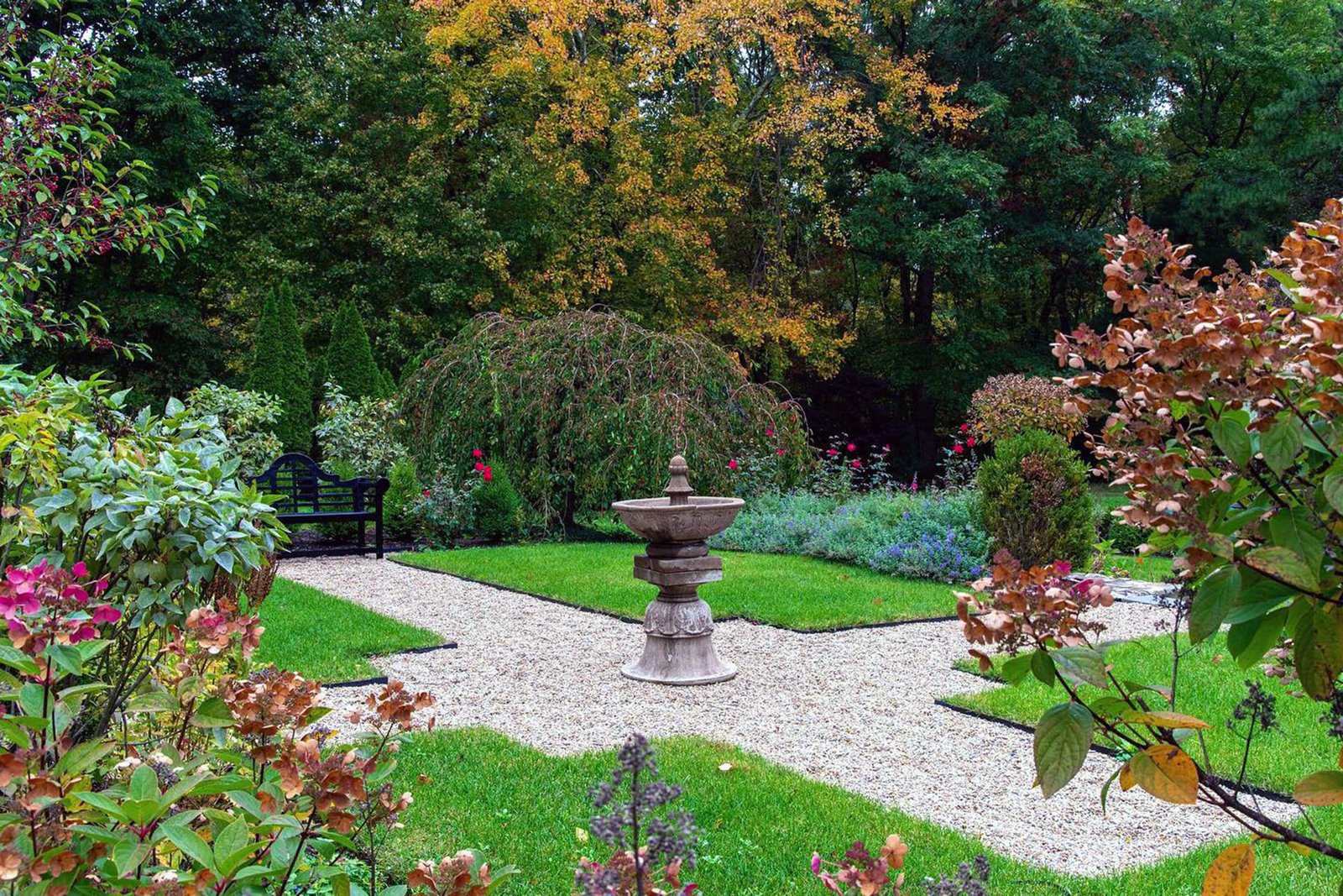 A classic stone garden urn lines the gravel path, providing structure and scale while reinforcing the formal rhythm of the surrounding landscape design.