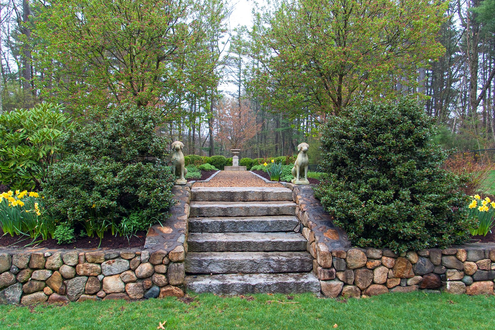 This formal garden stone statue anchors symmetrical steps, lending a sense of refinement and permanence to an estate-style landscape with strong architectural lines.