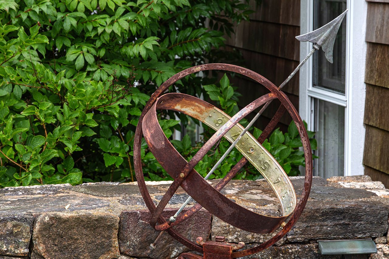 A weathered metal armillary sphere crowns a stone wall, introducing classical geometry and sculptural weight while reinforcing the garden’s sense of age and permanence.