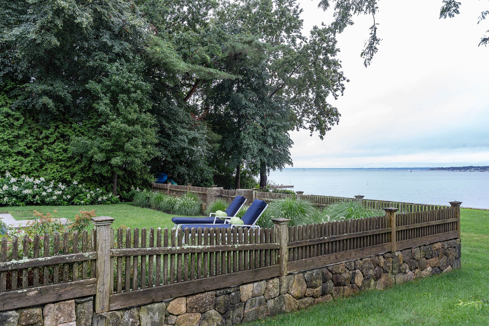 A coastal wood picket fence complements stone walls in Manchester-by-the-Sea, defining space without blocking ocean breezes.