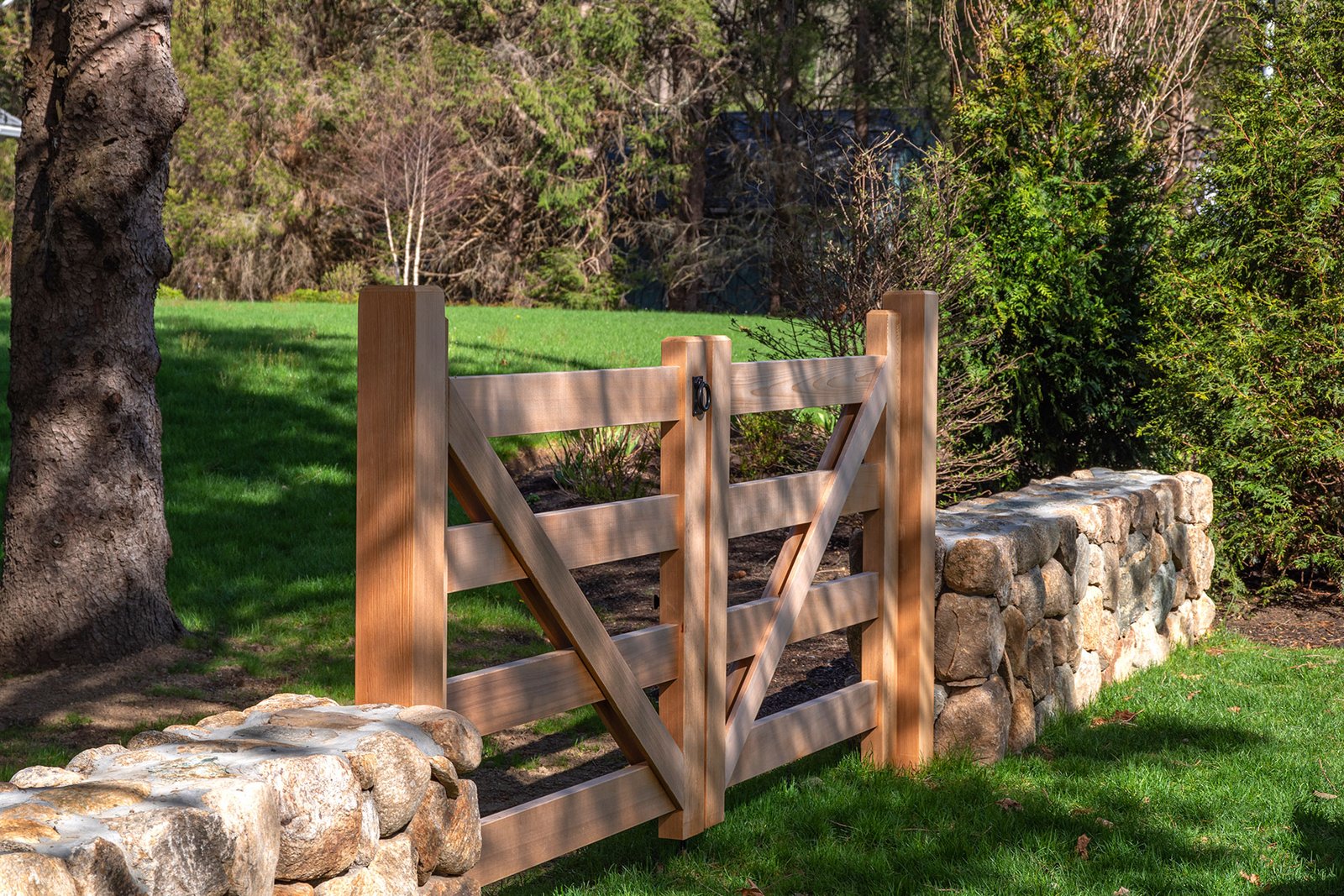 Custom cedar gates framed by granite walls in Lincoln create a refined garden entrance built to last.