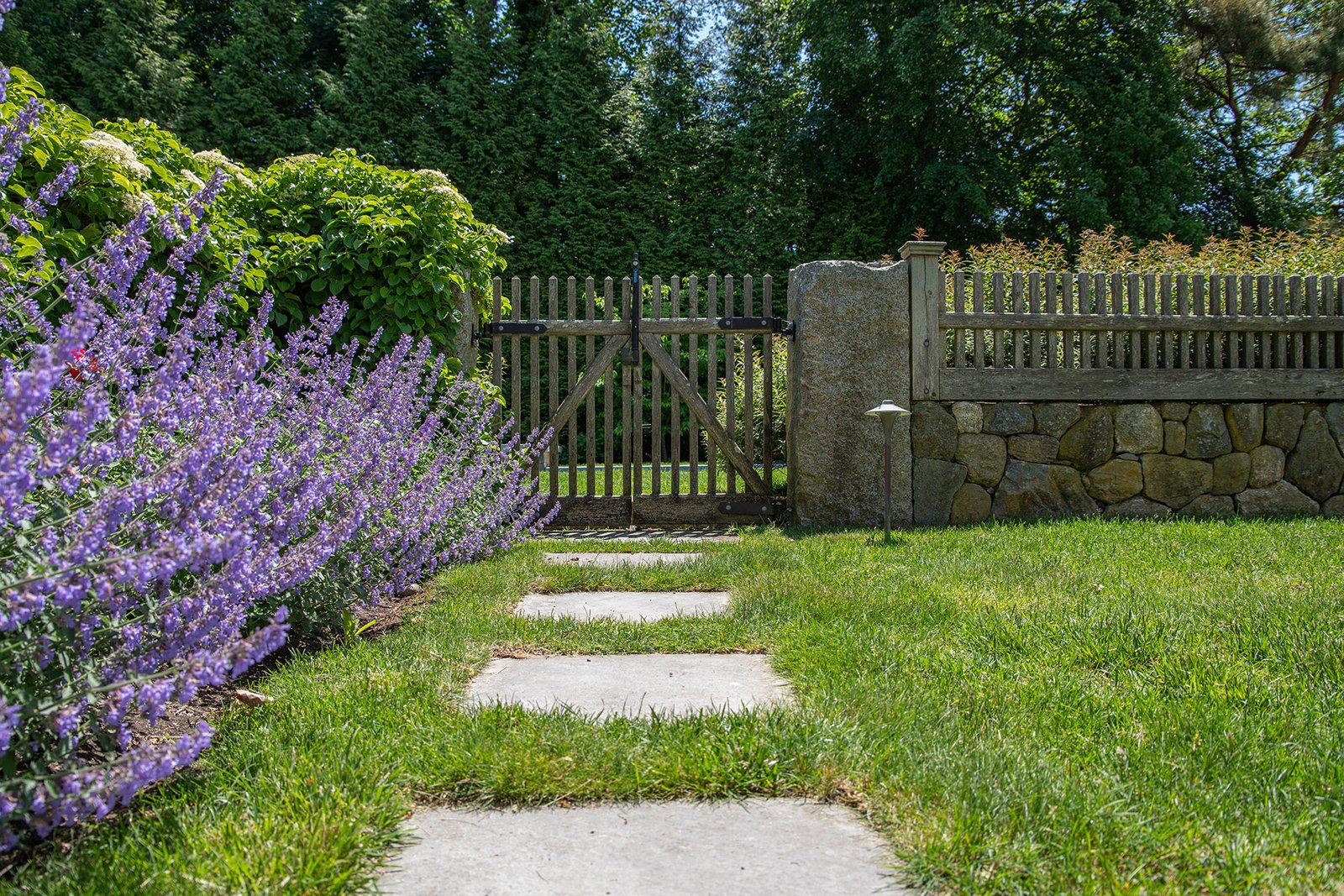 This weathered wood gate softens a stone wall in Weston, creating a functional garden entry with understated character.