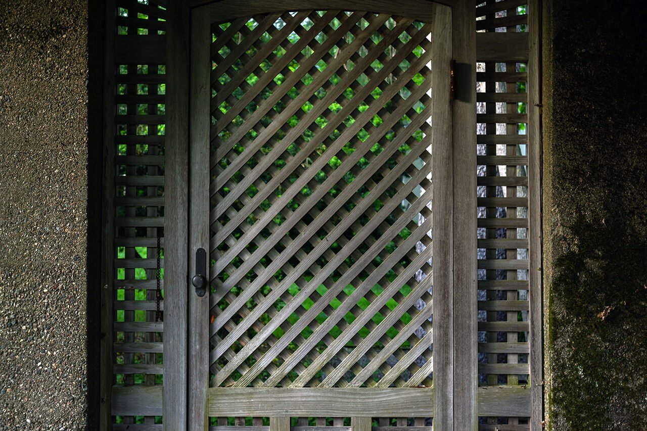 A lattice-top wood door adds texture and charm to a shaded entry, offering enclosure without blocking light or airflow.