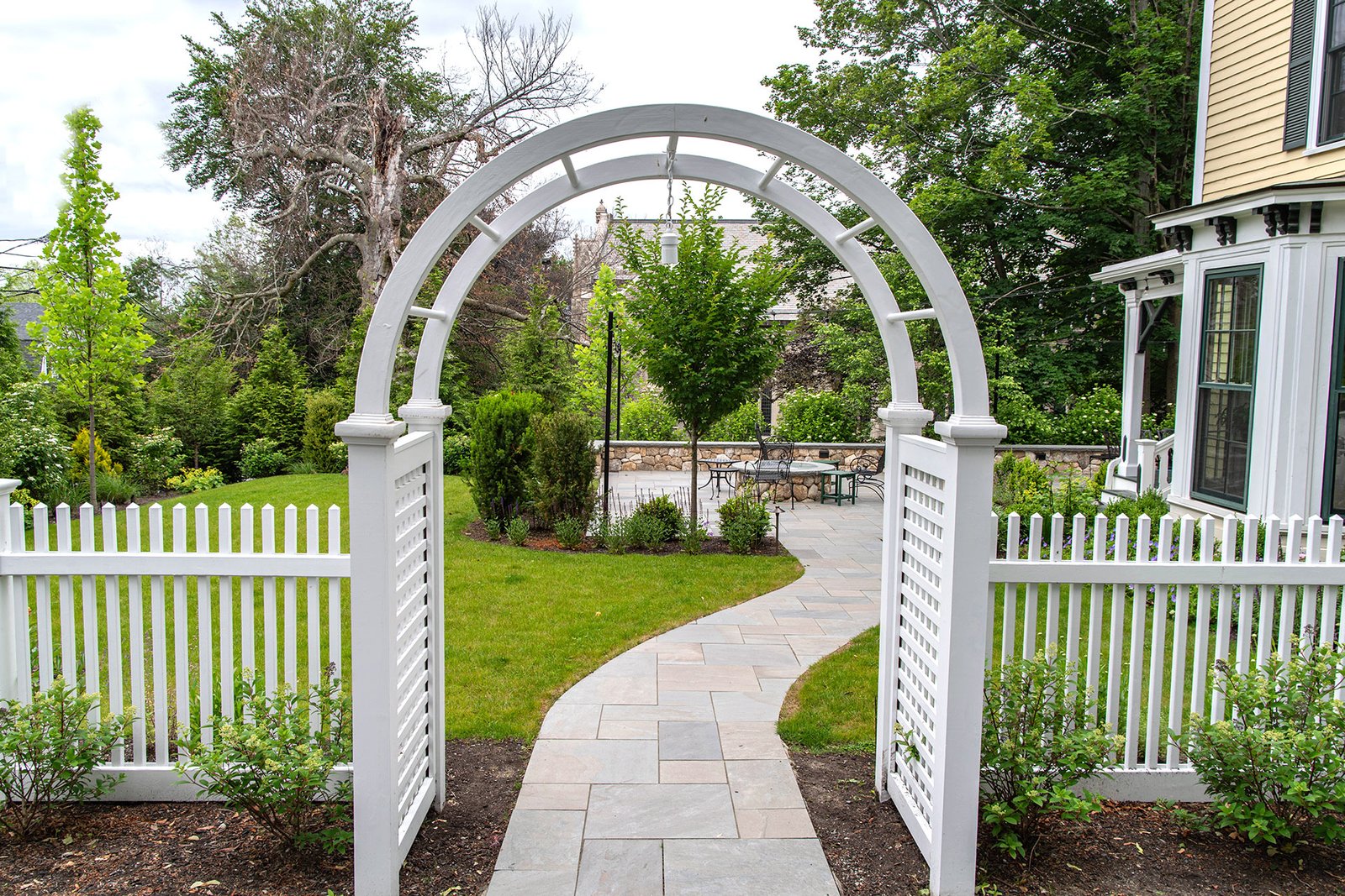 An arched white arbor paired with bluestone adds elegance to this Wellesley entry while clearly guiding foot traffic.