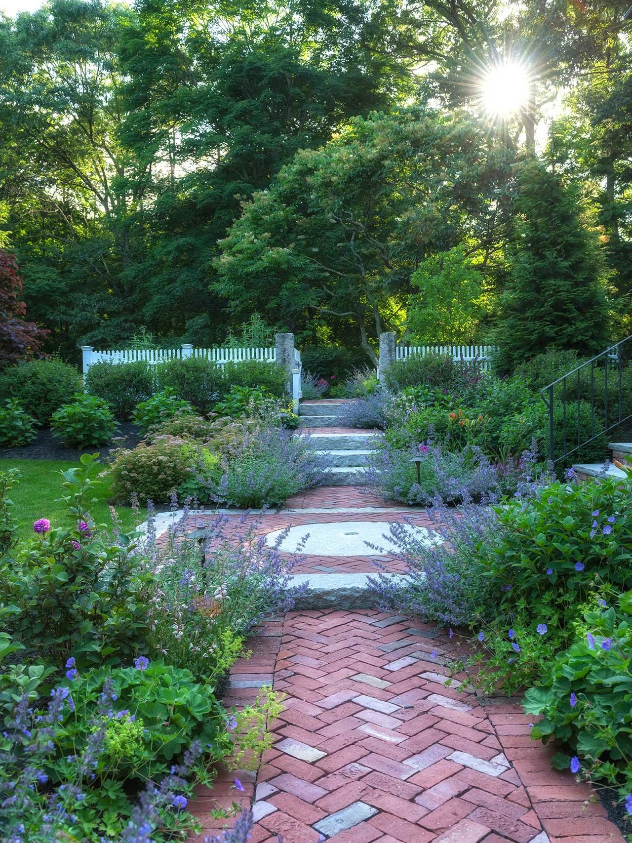 Lincoln, MA - Colorful perennial beds pull you along an inviting herringbone pattern walkway complete with an antique granite millstone focal piece.