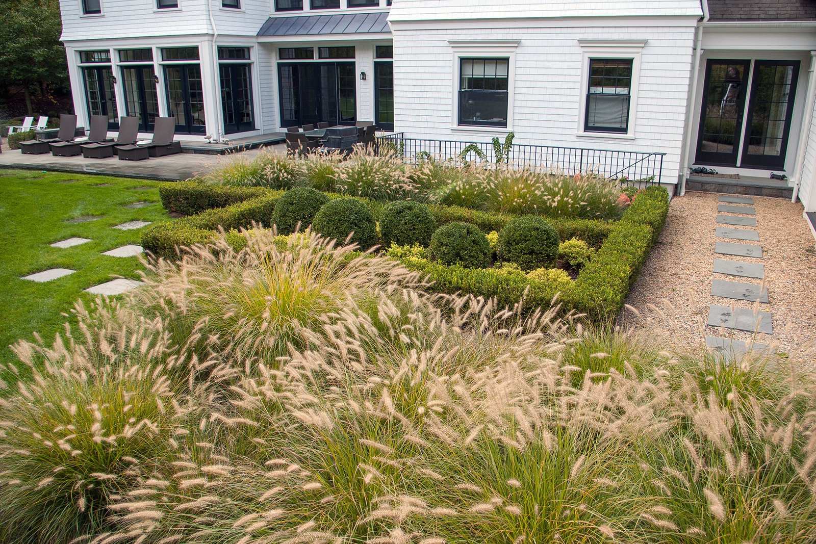 Structured garden borders pair ornamental grasses with boxwood in Dover, balancing crisp lines with soft texture for a polished residential landscape.